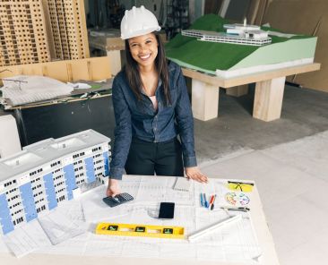 happy-african-american-lady-safety-helmet-standing-near-model-building (Demo) (Demo)
